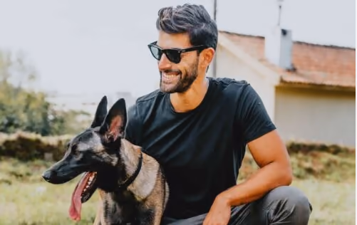 Treinador da Train your Dog ao ar livre, agachado ao lado de um pastor-belga malinois